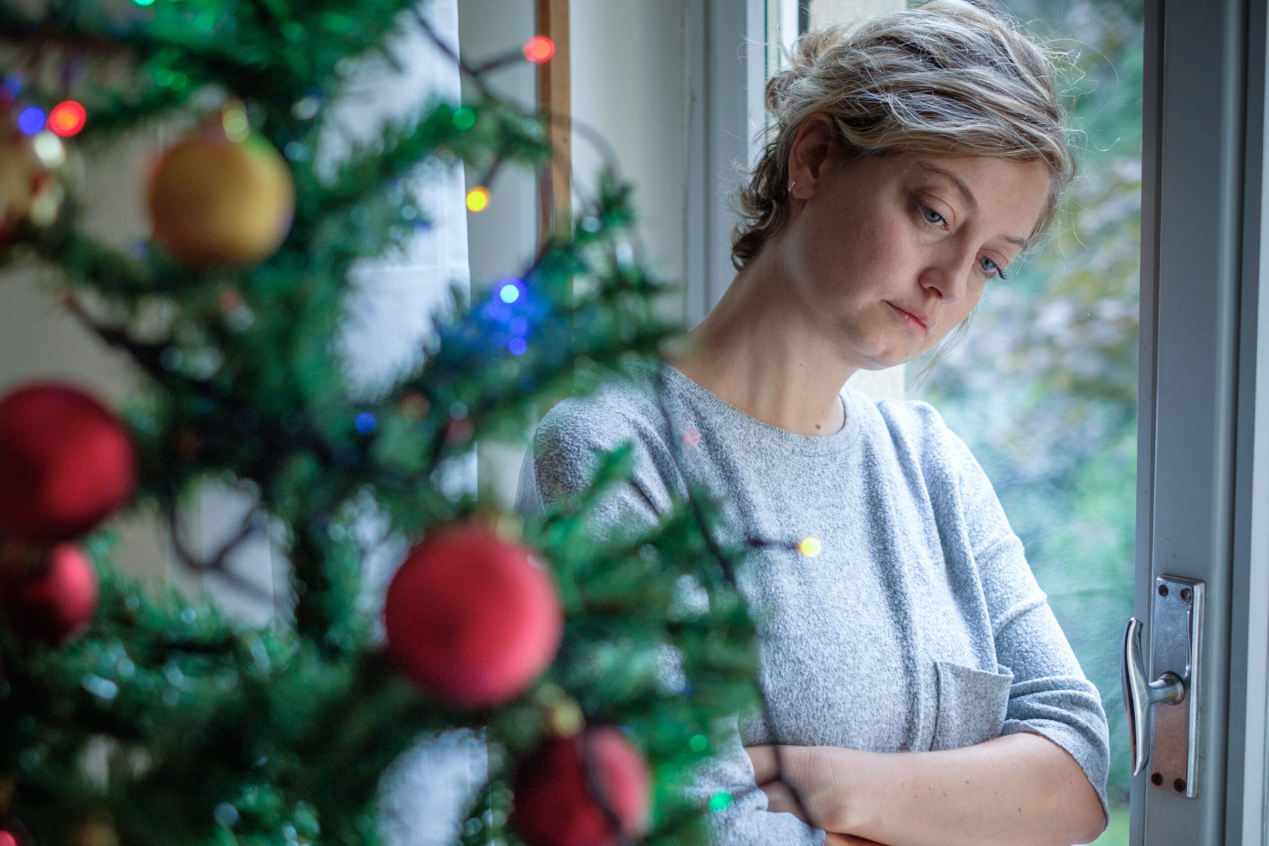 Woman going through a divorce during the holidays sad by a Christmas tree